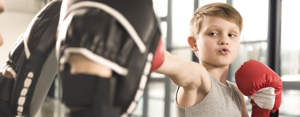 boks dla dzieci - chłopiec w rękawicach uderza łapy trenera