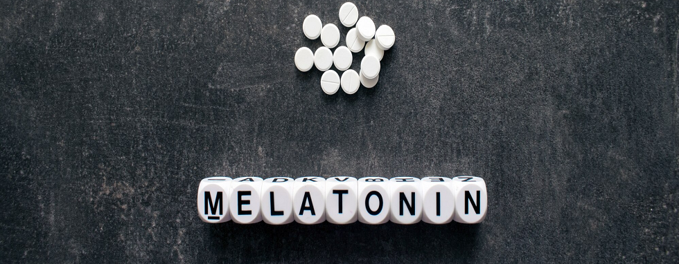 melatonina - białe pigułki i napis melatonina na czarnym tle